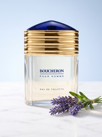 Boucheron Pour Homme Eau de Toilette 100 ml - Flakon mit Goldkappe und blauer Kuppel auf hellem Marmor mit Lavendel