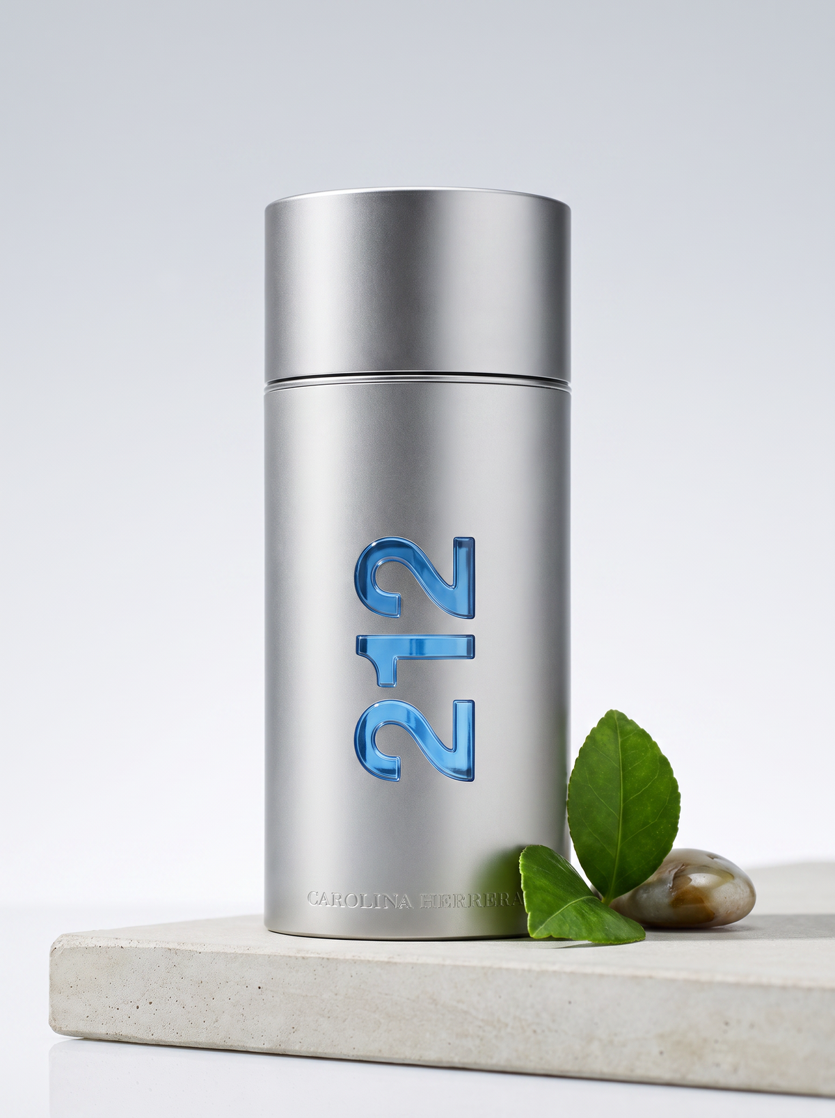 Carolina Herrera 212 Men Eau de Toilette 50 ml - silberner Flakon auf hellem Beton mit gruenen Blaettern