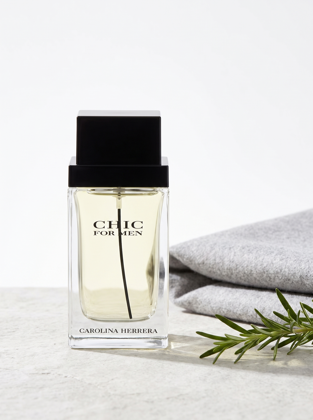 Carolina Herrera Chic for Men Eau de Toilette 100 ml - klarer Flakon auf hellem Stein mit Rosmarin