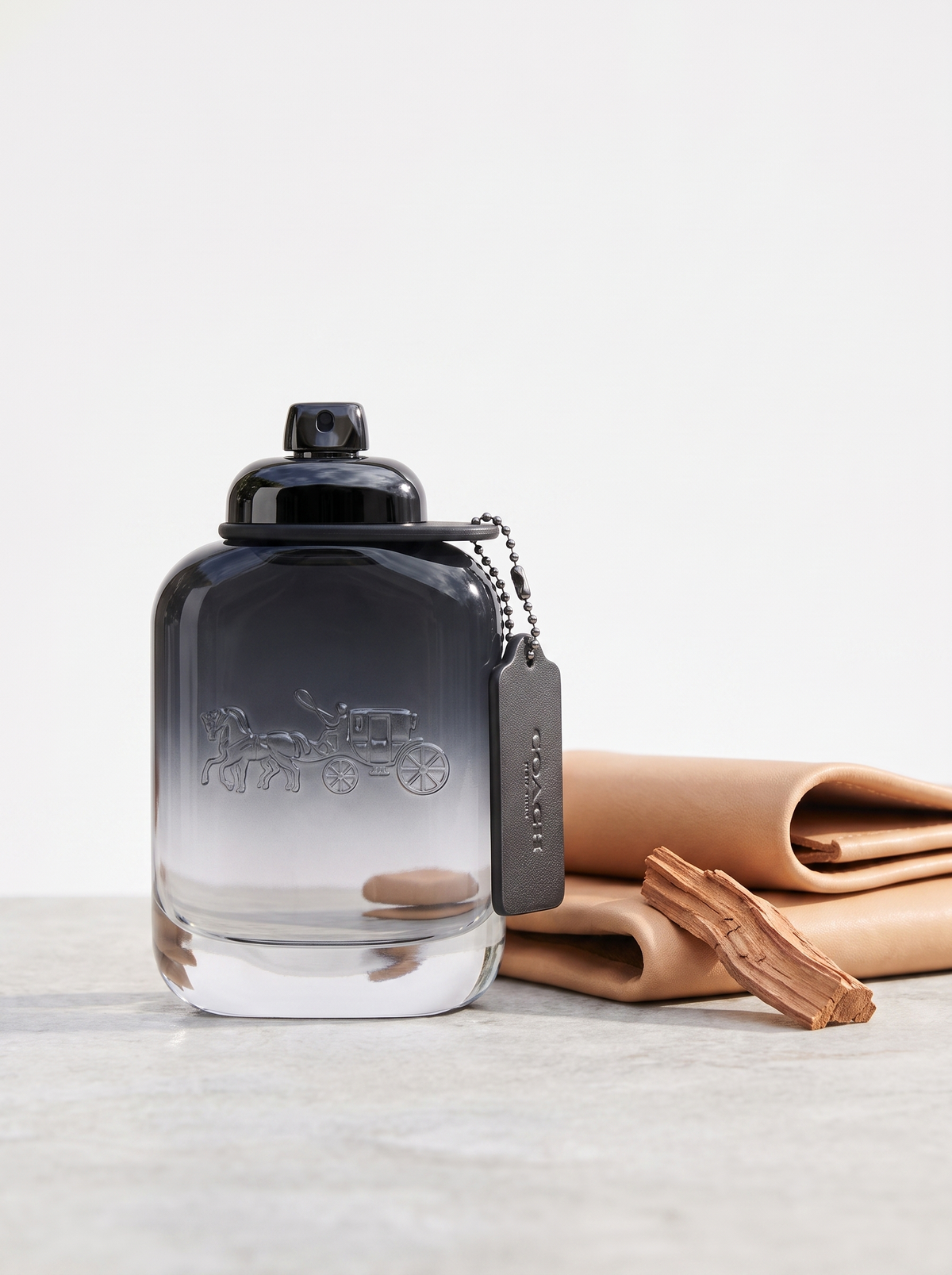 Coach for Men Eau de Toilette 100 ml - Flakon mit Lederanhaenger auf hellem Stein mit Zedernholz