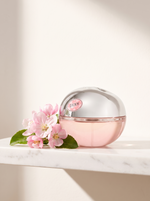 DKNY Be Delicious Fresh Blossom Eau de Parfum 100 ml - rosa Apfel-Flakon auf weissem Marmor mit Apfelblueten