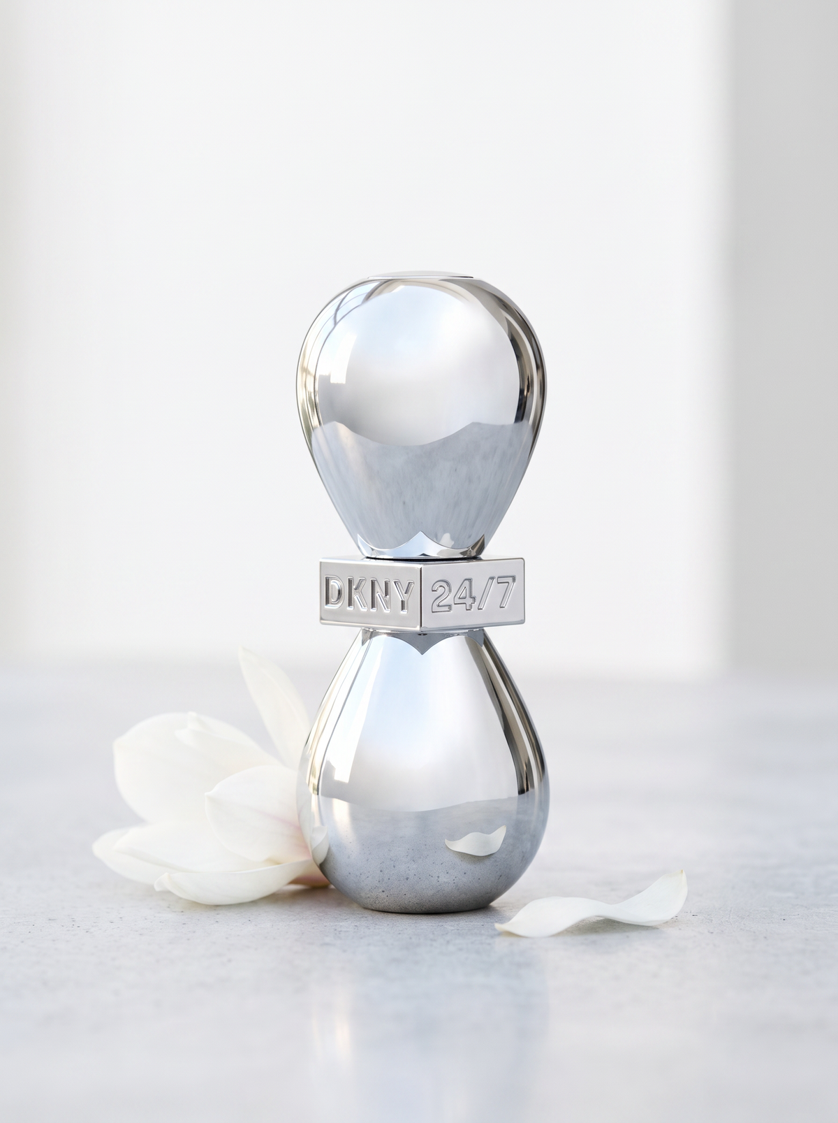 DKNY 24/7 Eau de Parfum 50 ml - Chrom-Flakon auf hellem Beton mit weisser Magnolie