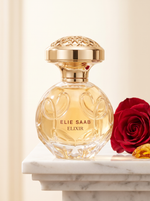 Elie Saab Elixir Eau de Parfum 50 ml - goldener Flakon auf weissem Marmor mit roter Rose