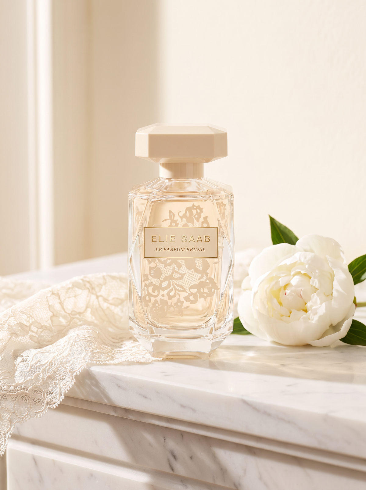 Elie Saab Le Parfum Bridal Eau de Parfum 90 ml - cremefarbener Flakon auf weissem Marmor mit Spitze und Pfingstrose