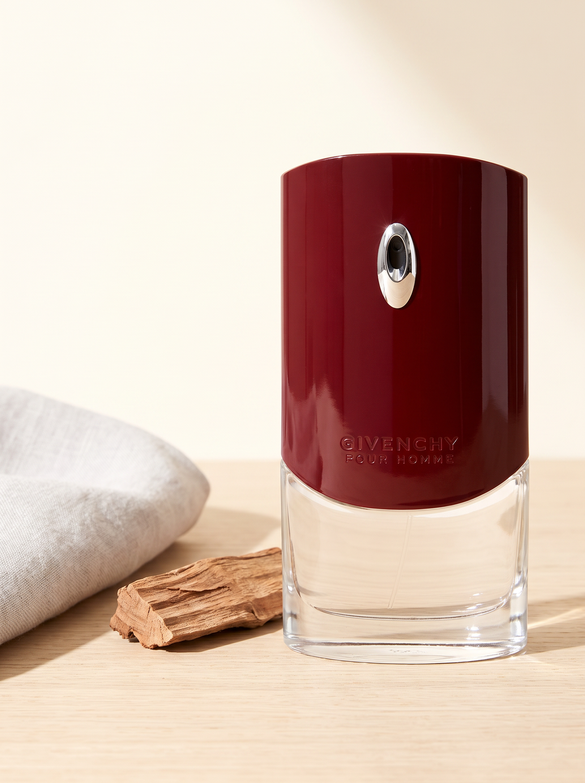 Givenchy Pour Homme Eau de Toilette 100 ml - weinroter Flakon auf hellem Eichenholz mit Sandelholz