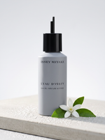 Issey Miyake L Eau d Issey Eau de Parfum Intense Nachfuellung 150 ml - Flakon auf hellem Beton mit weisser Bluete