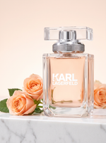 Karl Lagerfeld Eau de Parfum 85 ml - Flakon mit Nietenkragen auf hellem Marmor mit pfirsichfarbenen Rosen