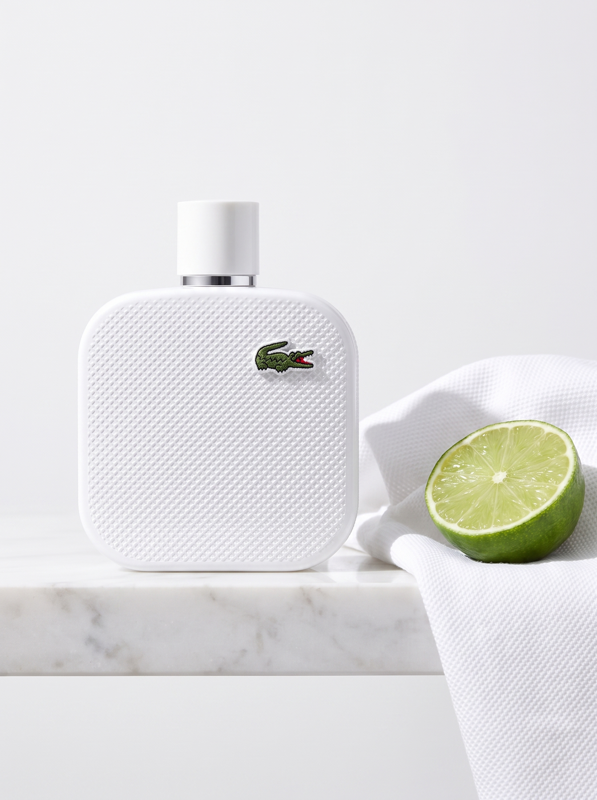 Lacoste L.12.12 Blanc Eau de Toilette 100 ml - weisser Pique-Flakon auf weissem Marmor mit Limette