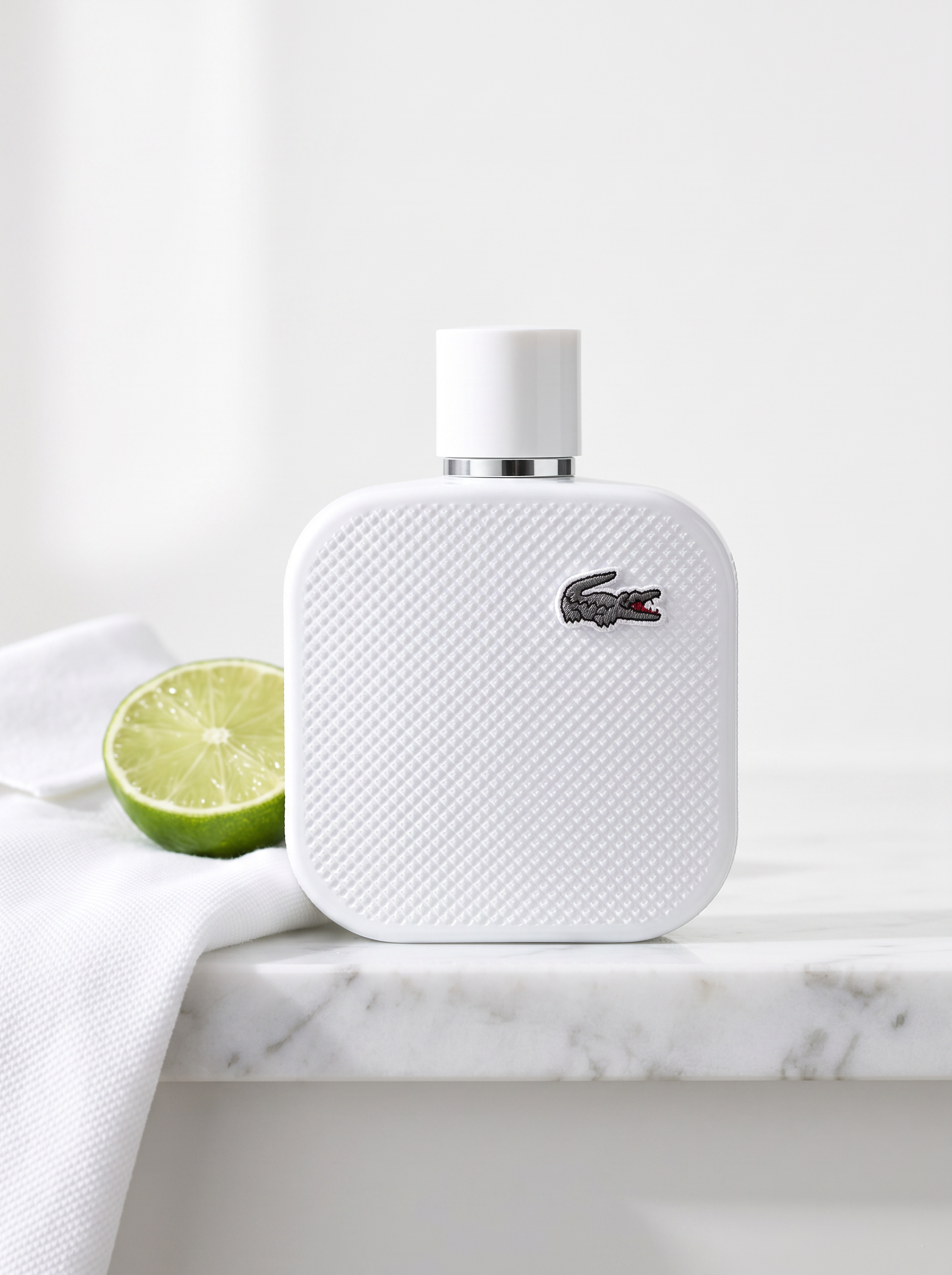 Lacoste L.12.12 Blanc Eau de Parfum 50 ml - weisser Pique-Flakon auf weissem Marmor mit Limette