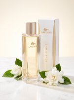 Lacoste Pour Femme Eau de Parfum 90 ml - Flakon mit Verpackung auf hellem Marmor mit weissen Blueten