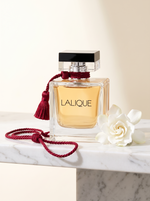 Lalique Le Parfum Eau de Parfum 100 ml - Flakon mit roter Seidenquaste auf weissem Marmor mit Gardenie