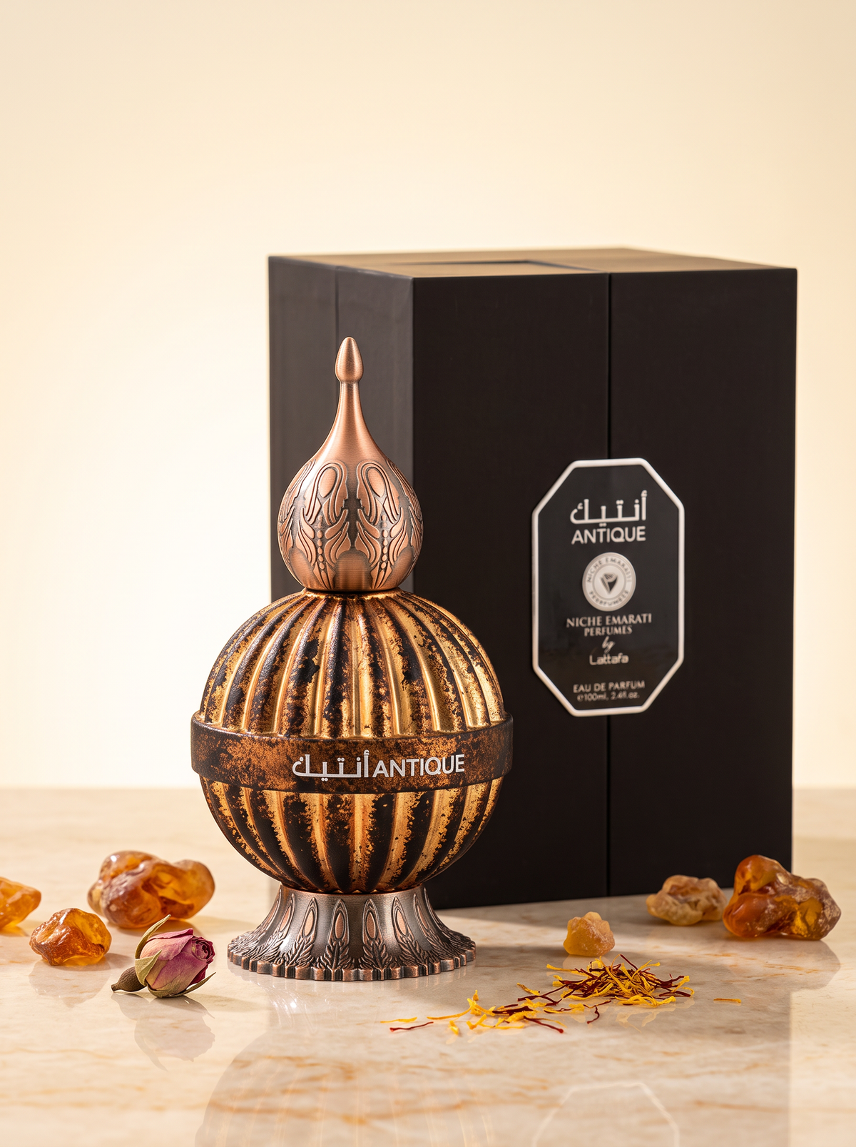 Lattafa Niche Emarati Antique Eau de Parfum 100 ml - verzierter Flakon mit Verpackung auf hellem Sandstein mit Bernstein und Safran