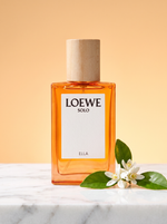 Loewe Solo Ella Eau de Parfum 30 ml - oranger Flakon mit Holzdeckel auf hellem Marmor mit Orangenblueten