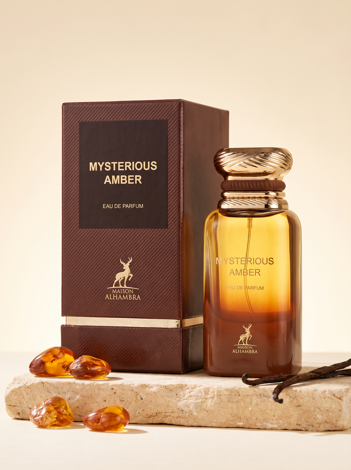 Maison Alhambra Mysterious Amber Eau de Parfum 100 ml - Flakon mit Verpackung auf Sandstein mit Bernstein und Vanille