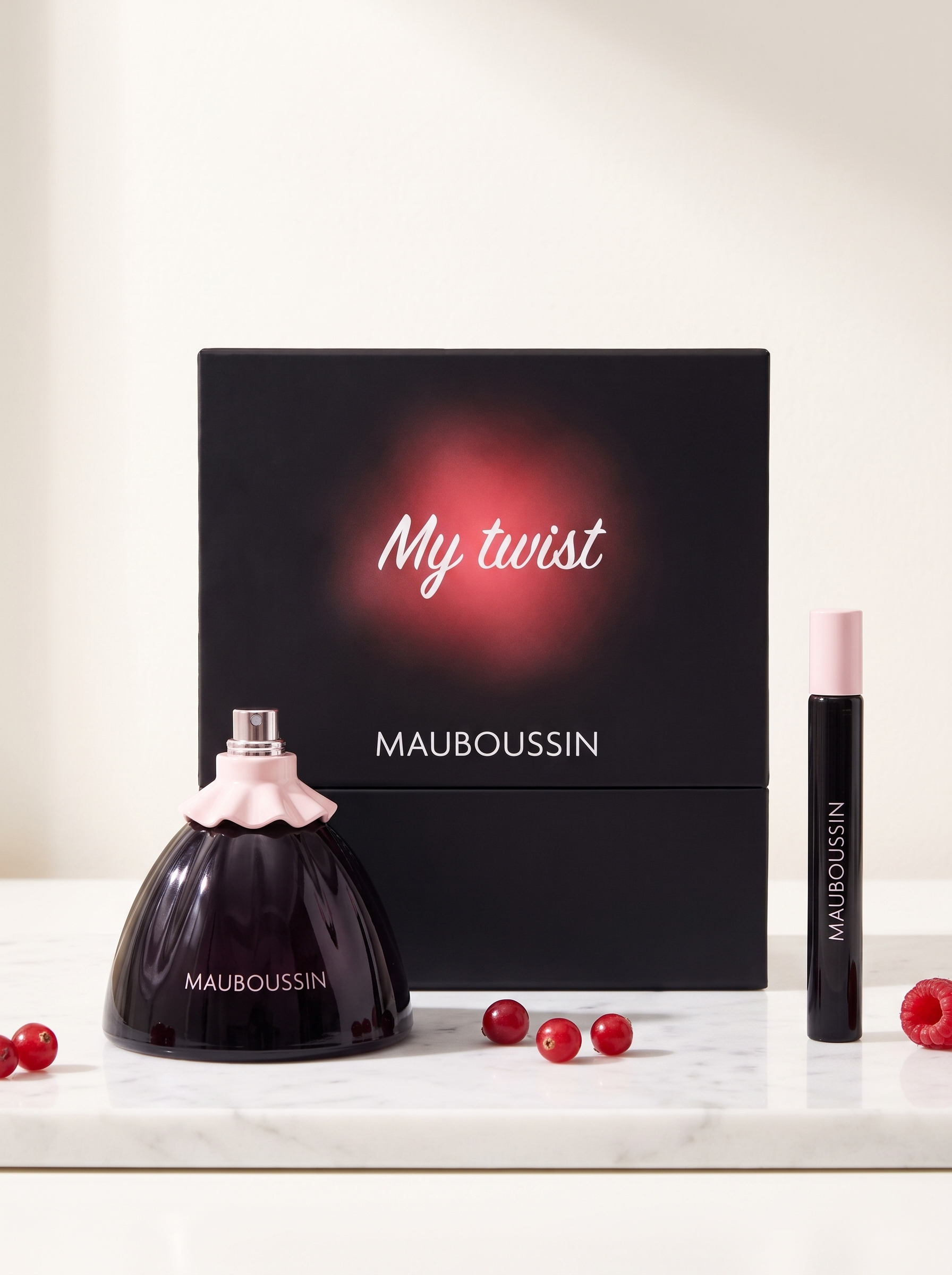 Mauboussin My Twist Eau de Parfum Geschenkset - dunkler Flakon mit Reisespray auf weissem Marmor mit roten Beeren