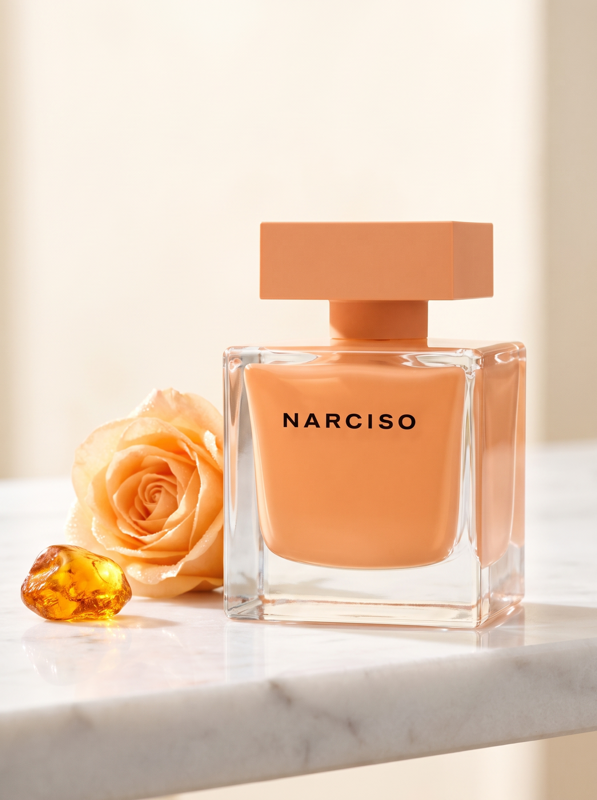Narciso Rodriguez Narciso Ambree Eau de Parfum 90 ml - aprikosenfarbener Flakon auf weissem Marmor mit Rose und Bernstein