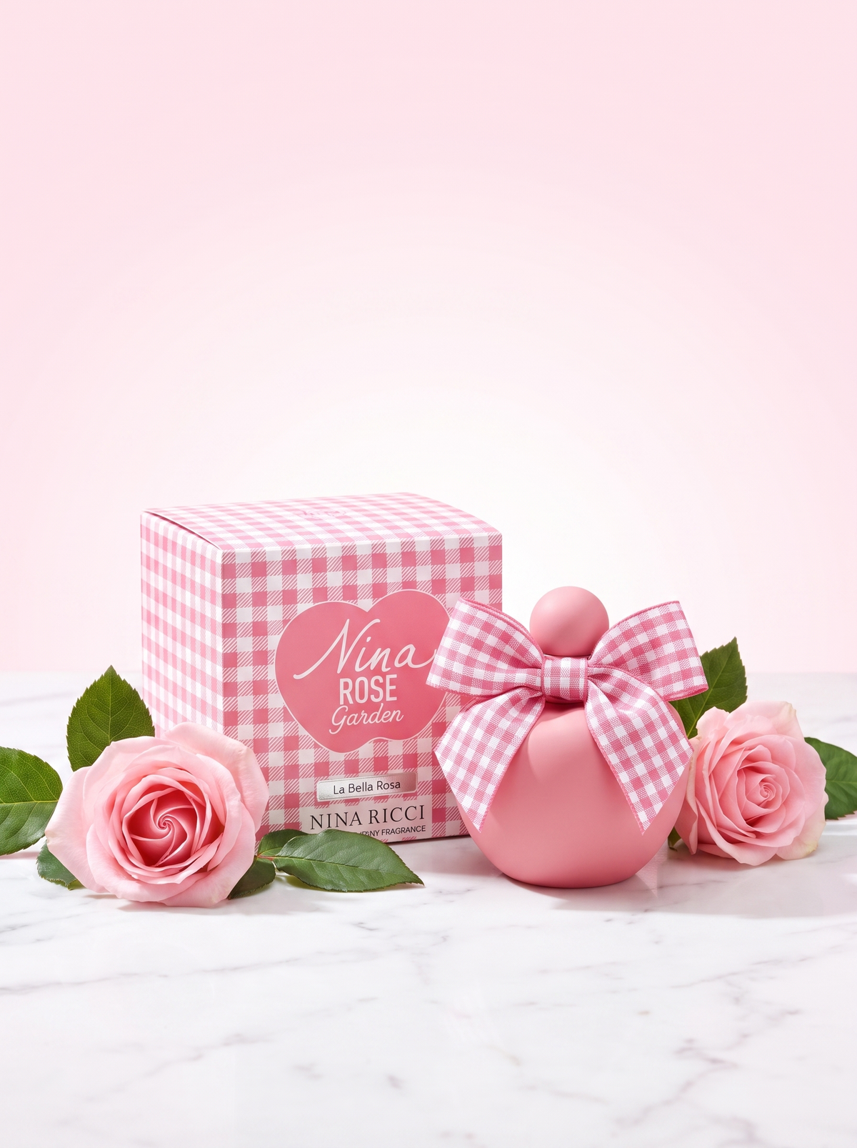 Nina Ricci Nina Rose Garden Eau de Toilette 50 ml - rosa Apfelflakon mit Schleife und Verpackung auf hellem Marmor mit Rosen