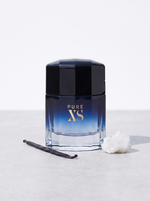 Rabanne Pure XS Eau de Toilette 100 ml - blau-schwarzer Flakon auf hellem Beton mit Vanille