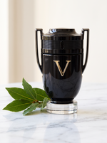 Rabanne Invictus Victory Eau de Parfum 100 ml - schwarzer Pokal-Flakon auf weissem Marmor mit Lorbeer