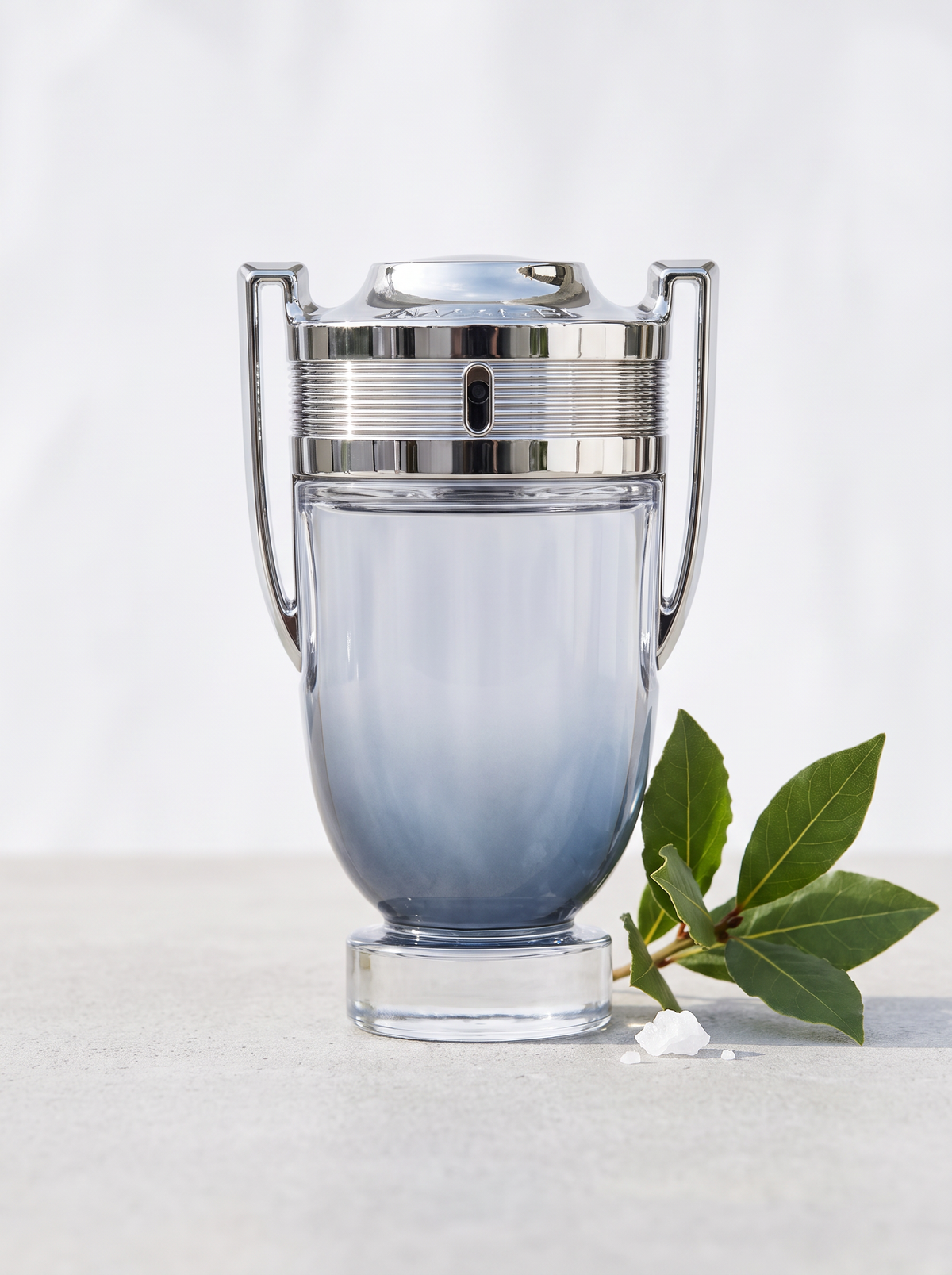 Rabanne Invictus Eau de Toilette 200 ml - Pokal-Flakon auf hellem Beton mit Lorbeer und Meersalz
