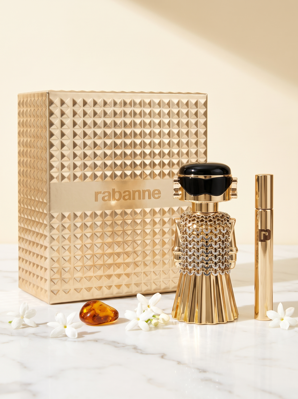 Rabanne Fame Eau de Parfum Geschenkset - goldener Figur-Flakon mit Reisespray auf weissem Marmor mit Jasmin