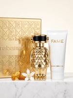 Paco Rabanne Fame Intense Geschenkset - goldener Figur-Flakon mit Bodylotion und Verpackung auf hellem Marmor