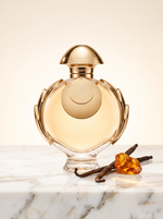 Rabanne Olympea Elixir Eau de Parfum 80 ml - goldener Flakon auf hellem Marmor mit Vanilleschoten und Bernstein