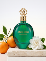 Roberto Cavalli Verde Assoluto Eau de Parfum 75 ml - gruener Flakon auf hellem Travertin mit Orangen und Gardenie