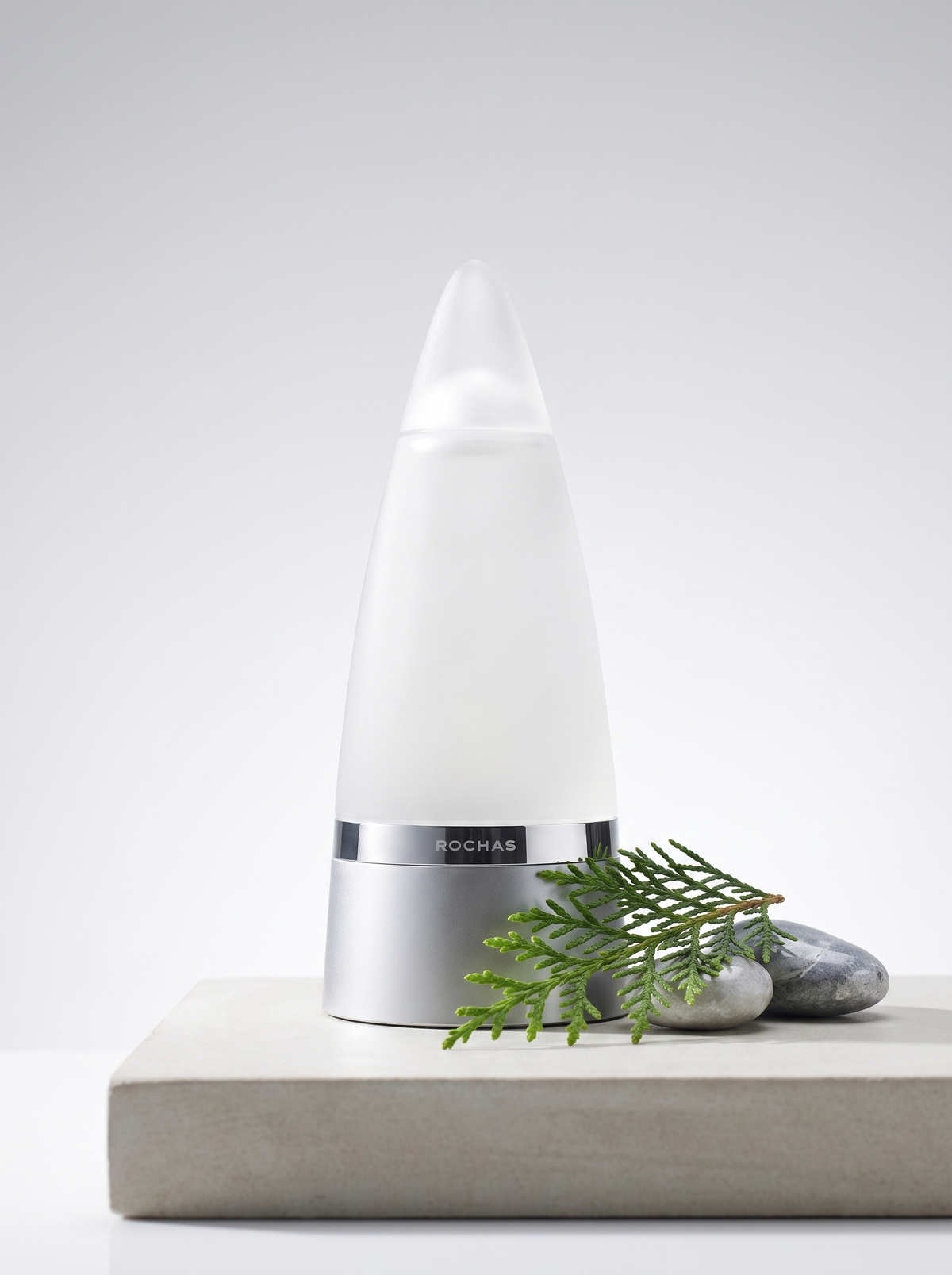 Rochas Man Eau de Toilette 100 ml - weisser Kegelflakon auf hellem Beton mit Zedernzweig