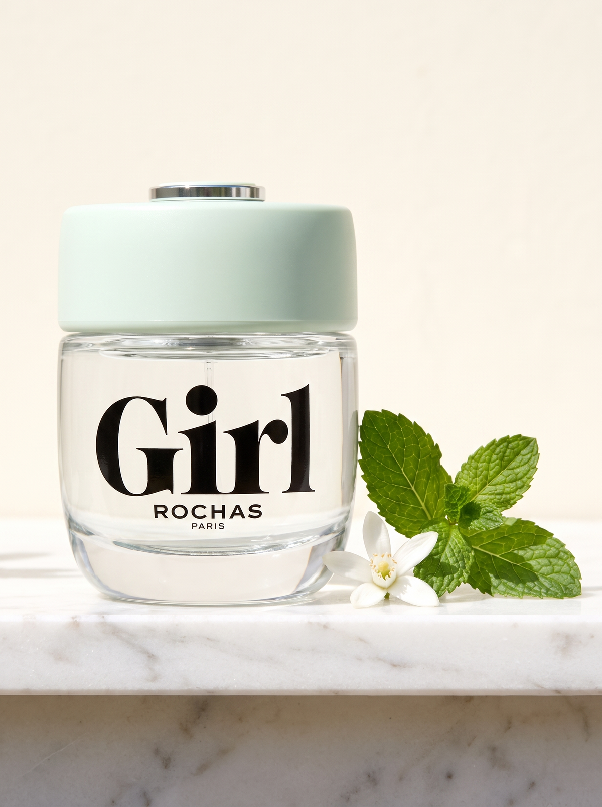 Rochas Girl Eau de Toilette 75 ml - klarer Flakon mit mintgruener Kappe auf weissem Marmor mit Minze