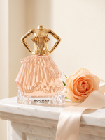 Rochas Audace Eau de Parfum 60 ml - Flakon in Kleidform auf weissem Marmor mit Pfirsichrose