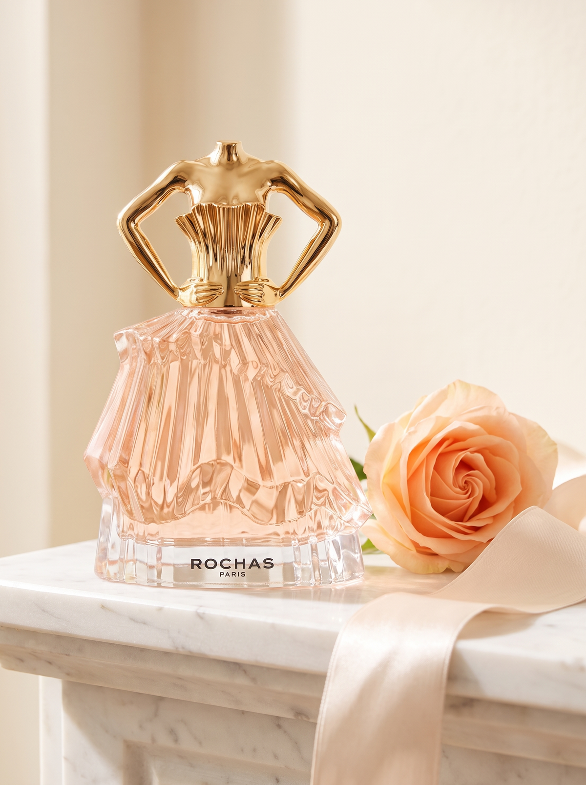 Rochas Audace Eau de Parfum 60 ml - Flakon in Kleidform auf weissem Marmor mit Pfirsichrose