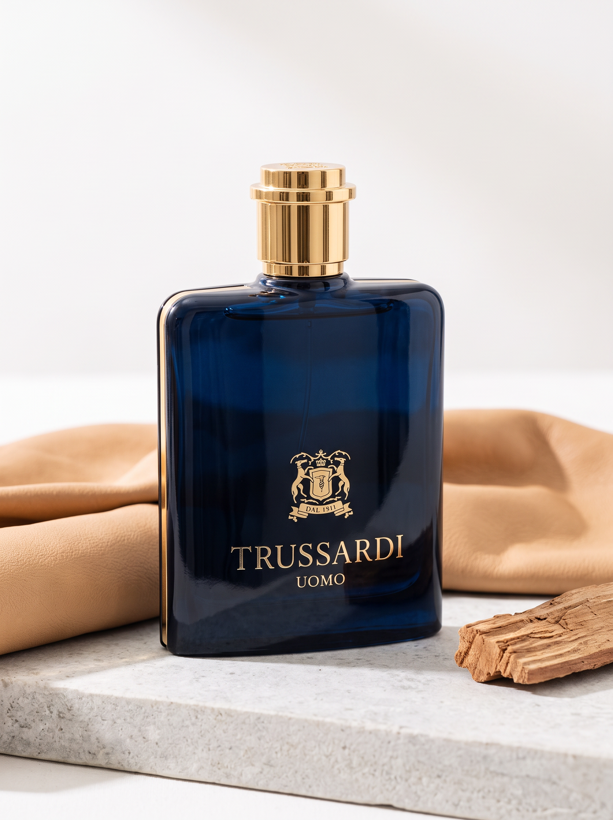 Trussardi Uomo Eau de Toilette 100 ml - blauer Flakon mit Goldkappe auf hellem Stein mit Leder und Zedernholz